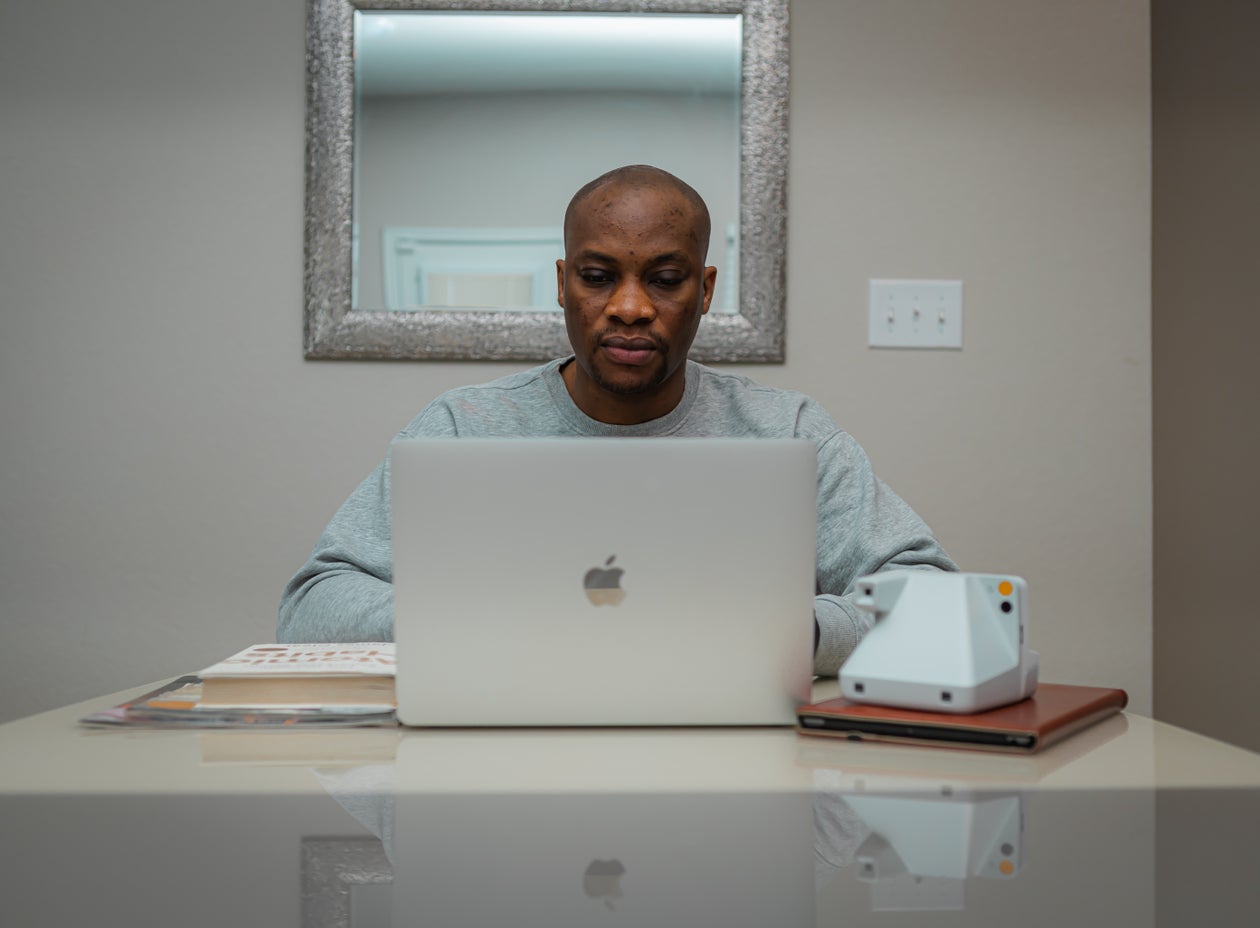 A man focused at his laptop at a clean desk with a notebook and instant camera beside him